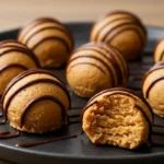 No-Bake Peanut Butter Cheesecake Balls neatly arranged on a matte black plate, drizzled with chocolate, on a wooden table.