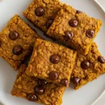 A pumpkin chocolate chip oatmeal bars on a white plate with cinnamon sticks.