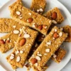 Almond coconut protein bars with visible coconut flakes and chopped almonds displayed on a white ceramic plate from a top-down perspective