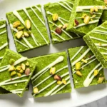 Bright Matcha Green Tea Protein Bars with white chocolate drizzle and pistachio pieces displayed on a white ceramic plate