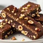 Dark brown mocha espresso protein bars topped with crushed hazelnuts, arranged on a white plate and photographed from above