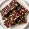 Dark brown mocha espresso protein bars topped with crushed hazelnuts, arranged on a white plate and photographed from above