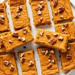 Orange-tinted pumpkin spice protein bars garnished with chopped pecans, neatly arranged on a white plate