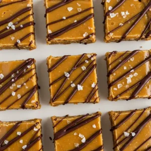 Golden brown salted caramel protein bars with dark chocolate drizzle and sea salt crystals, arranged on a white plate