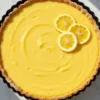 A homemade Easy Lemon Tart in a 9-inch round tart pan with a removable bottom, featuring a buttery, flaky crust layered with smooth, vibrant lemon curd filling. Topped with a light dusting of powdered sugar and fresh lemon slices for garnish.