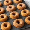 Homemade mini apple cider donuts in donut pan with golden-brown baked rings coated in sparkling cinnamon-sugar on white marble surface