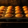 Mini pumpkin spice cupcakes baking in oven with golden-orange domed tops perfectly risen in mini muffin tin, illuminated by warm oven light