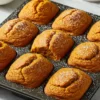 Homemade petite spiced pumpkin loaves in mini loaf pan with golden-orange spiced cake dusted with powdered sugar on white marble surface