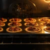 Tiny maple-pecan tartlets baking in oven with golden pastry shells and maple filling bubbling and setting, illuminated by warm oven light