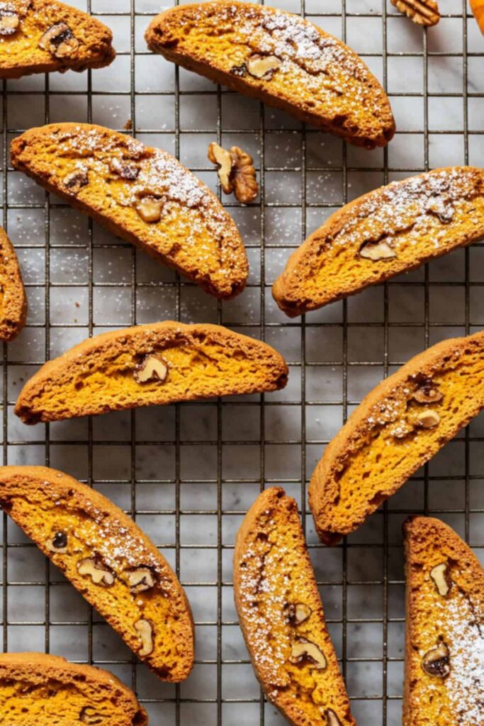 crispy pumpkin walnut biscotti arranged on a rustic wire cooling rack, showcasing pumpkin, warm spices, and toasted walnuts, with a delicate sprinkle of powdered sugar on top.