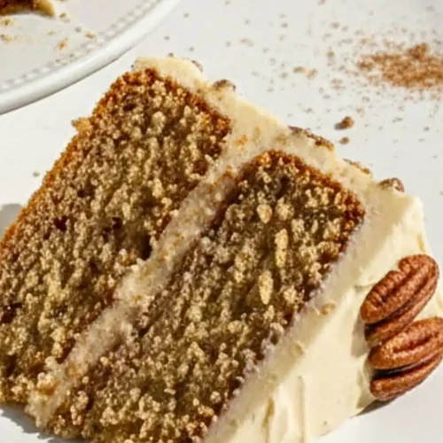 A Maple Pecan Cake, featuring two layers of golden-brown buttery cake with visible toasted pecan pieces, frosted with smooth maple buttercream and decorated with whole toasted pecans on top and pressed around the sides.