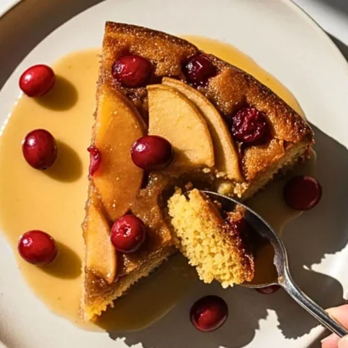 A slice of Apple Cranberry Upside-Down Cake on a cream ceramic dessert plate