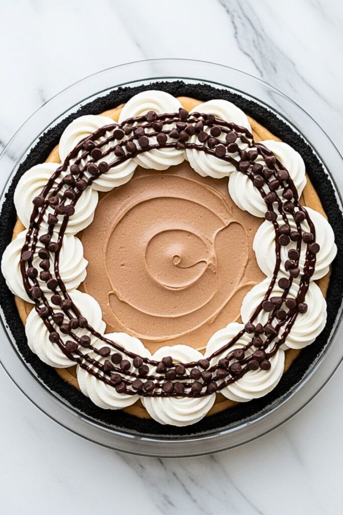 chocolate peanut butter pie in a glass pie dish on a clean white marbled table.