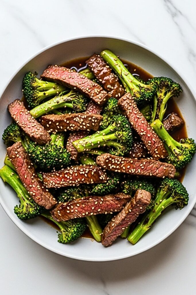beef and broccoli in a wide serving bowl on a clean white marbled table.